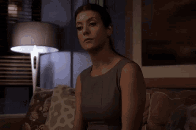 a woman in a grey dress sits on a couch in a dark room