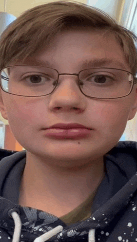 a young man wearing glasses and a hoodie is making a funny face .