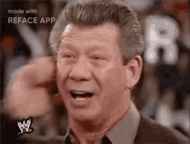 a man is laughing and covering his ears with his hand while wearing a wrestling shirt .