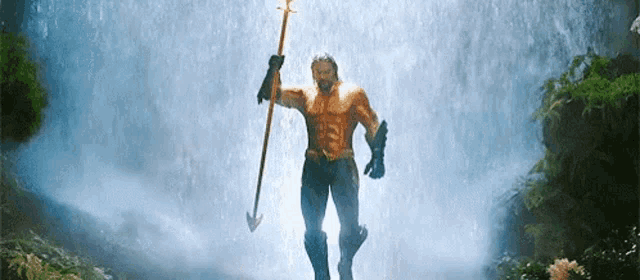 a man is standing in front of a waterfall holding a trident .