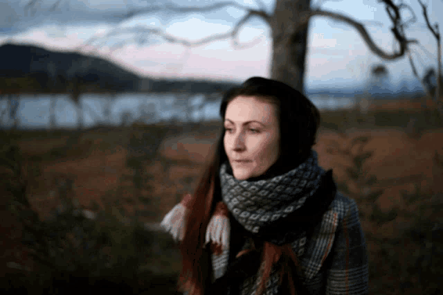 a woman wearing a scarf stands in front of a tree