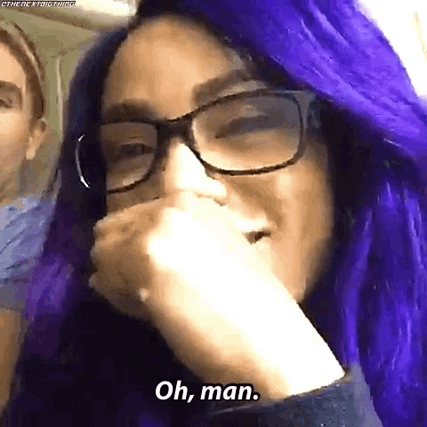 a woman with purple hair and glasses is covering her mouth with her hand and says oh man .