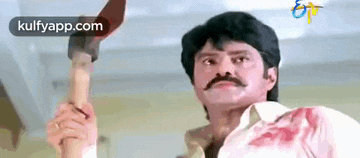 a man with a mustache is holding a bloody knife in his hand .