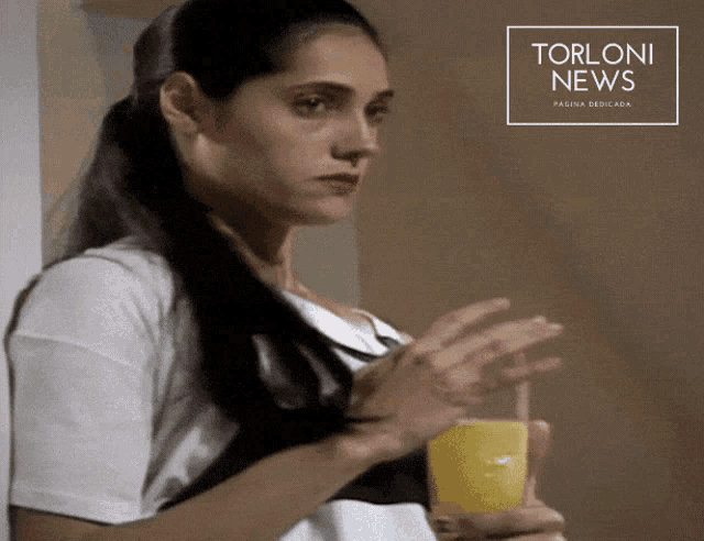 a woman is holding a glass of orange juice in front of a torloni news banner