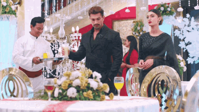 a group of people standing around a table with a waiter holding a tray of drinks