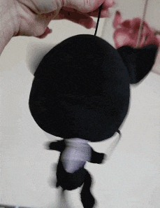 a person is holding a black stuffed animal with a string hanging from it