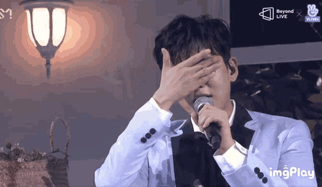 a man in a suit is covering his face with his hands while singing into a microphone with beyond live written in the corner