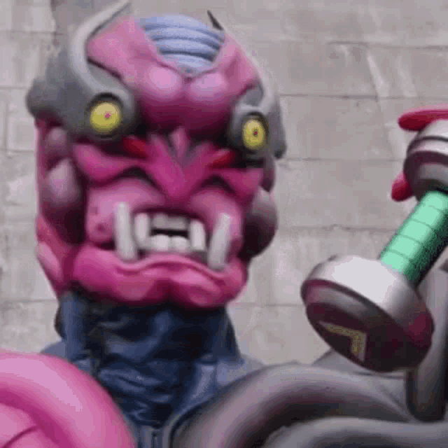 a pink monster is holding a green and silver dumbbell in his hand .