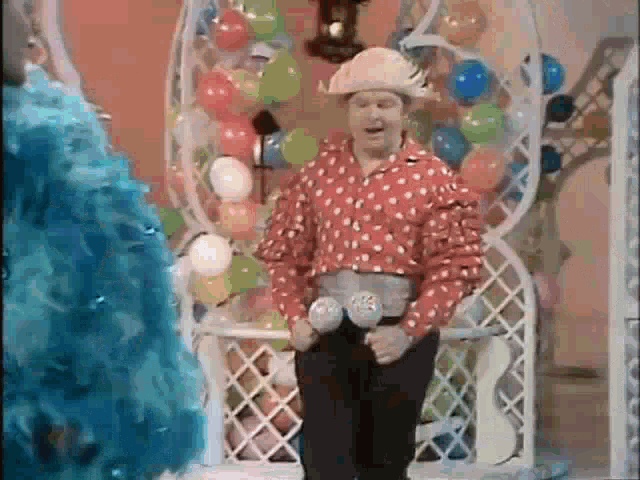 a man in a polka dot shirt and cowboy hat is standing in front of balloons and a chair .