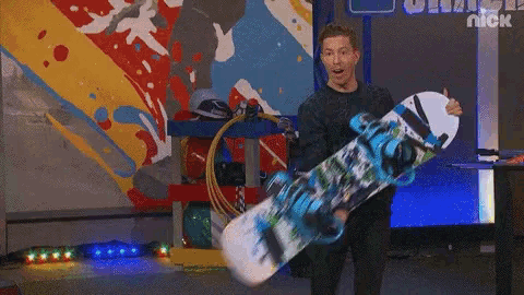 a man holding a snowboard in front of a wall that says nick on it