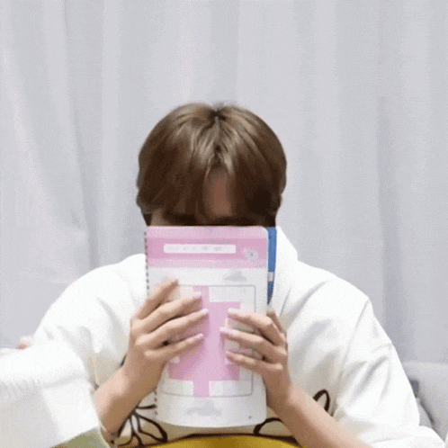 a person covering their face with a book that has the letter f on it