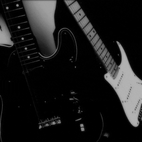 a black and white photo of two electric guitars on a dark background