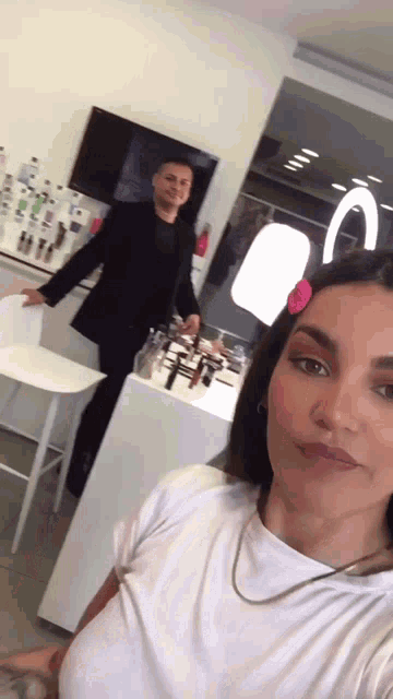 a woman in a white shirt is taking a selfie with a man standing behind her