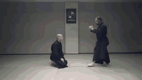 two men are practicing martial arts in a gym and one of them is kneeling down next to another man .