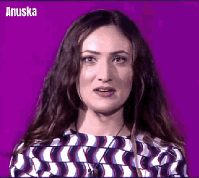 a woman with long hair is making a funny face in front of a purple background with the name anuska on it .