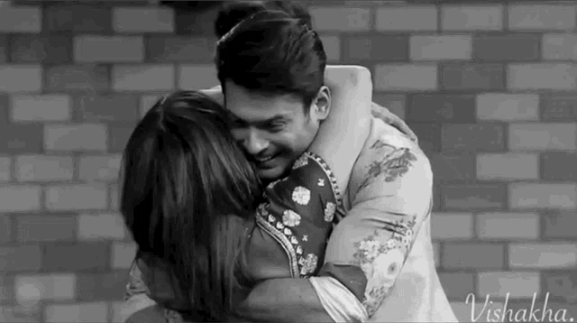 a man and a woman hugging each other in front of a brick wall .
