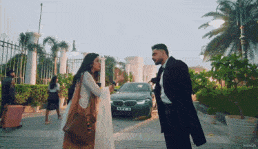 a man and a woman are standing in front of a bmw with a license plate that says mhv jt