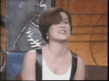 a woman wearing a white tank top and a black leather vest is making a funny face .