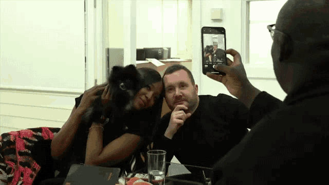 a man taking a picture of a woman and a dog with his phone
