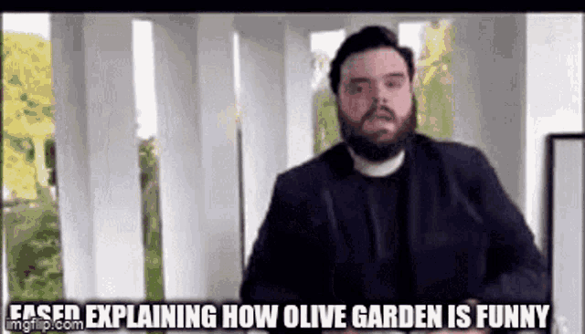 a man in a suit and tie is standing in front of a window and explaining how olive garden is funny .