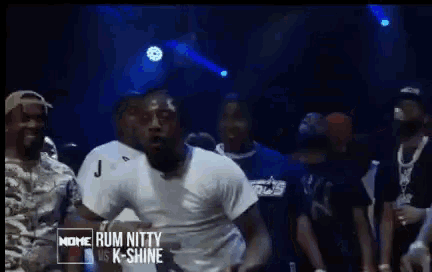 a man in a white shirt is dancing in front of a crowd and the words rum nitty vs k-shine are on the screen
