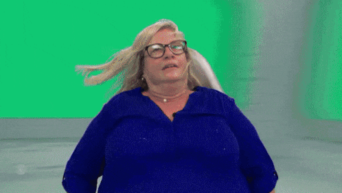 a woman wearing glasses and a blue shirt stands in front of a blue screen
