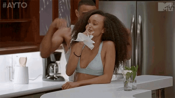 a woman in a bikini is sitting at a kitchen counter holding a napkin in her hand .