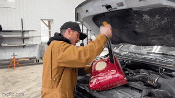 a man in a brown jacket is holding a bag under the hood of a car .