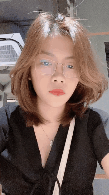 a woman wearing glasses and a black shirt is taking a selfie