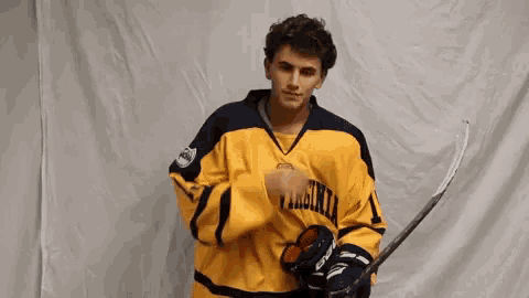 a young man in a yellow and black virginia hockey jersey is holding a hockey stick .