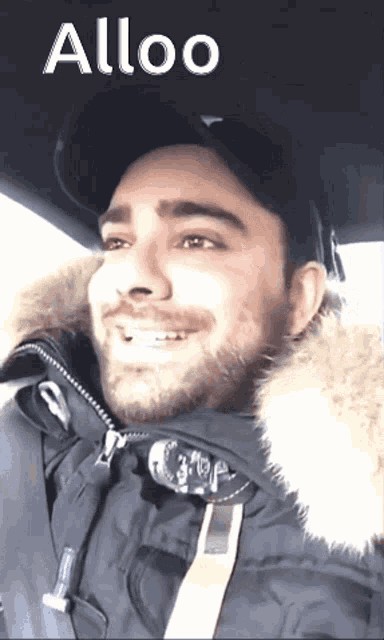 a man with a beard is smiling in a car with the word alloo on the bottom