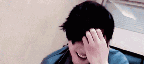 a person is covering their face with their hand while smiling .