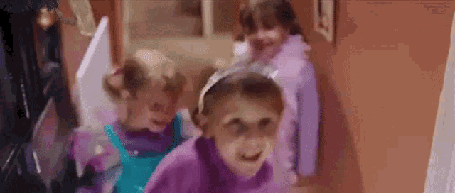 three little girls are walking down a hallway .