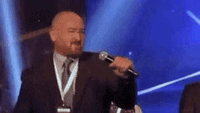 a man in a suit and tie is singing into a microphone with the word bit behind him .