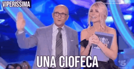 a man in a suit and tie stands next to a woman in a black dress and says una ciofeca on the screen