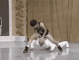 a man in a basketball jersey is wrestling another man in a white shirt .