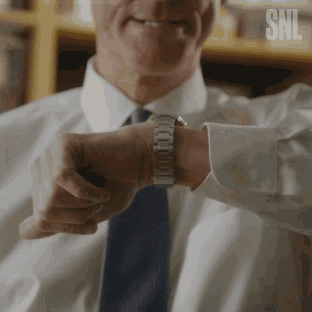 a man in a white shirt and blue tie is checking his watch and smiling