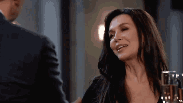a woman in a black dress is smiling while talking to a man in a suit .