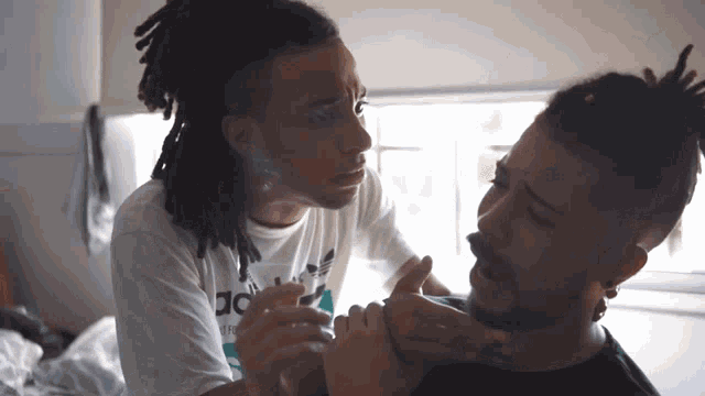 a man with dreadlocks is smoking a cigarette while another man holds his neck