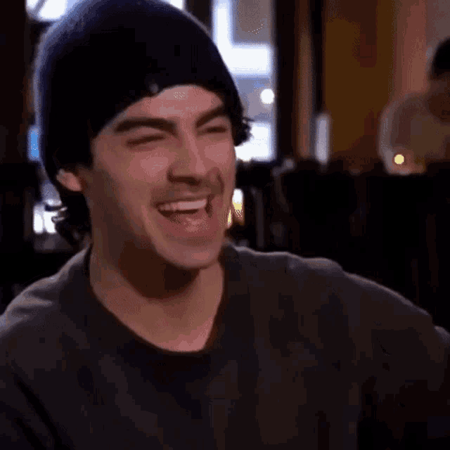 a man wearing a beanie is laughing with his eyes closed in a restaurant .