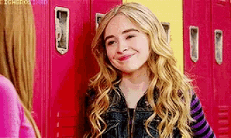 a girl with blonde hair is standing in front of a row of lockers and smiling .