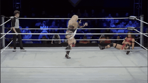 two women are wrestling in a ring with a referee standing in the background