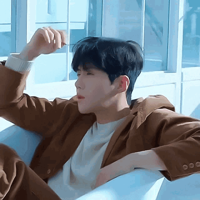 a young man in a brown jacket is laying on a white couch