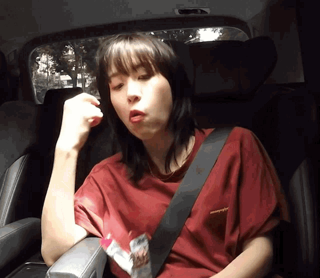 a woman wearing a red t-shirt that says ' abercrombie & fitch ' on it sits in a car