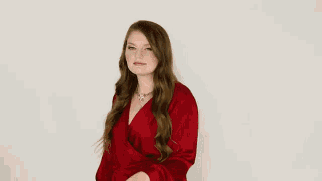 a woman in a red dress is standing in front of a white wall .