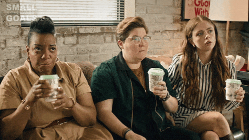 three women are sitting on a couch drinking coffee with a sign that says small goals behind them