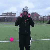 a man wearing a beanie is standing on a soccer field with a pink ball