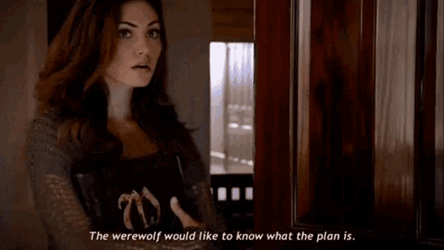 a woman is standing in front of a door holding a book and talking to a werewolf .