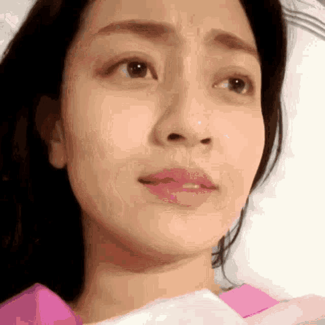a close up of a woman 's face with a pink shirt on looking at the camera .