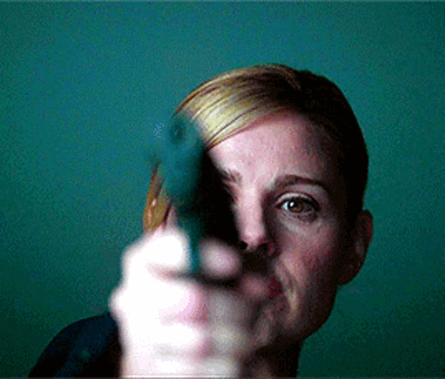 a woman pointing a gun at the camera with a blue background